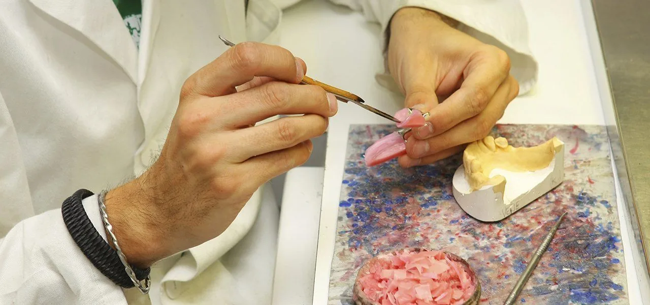 A dental technician shaping pink wax on a denture model at the bench